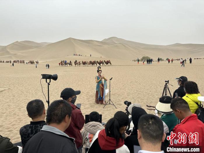 圖為2023年4月底，敦煌大漠“逐舞者”奧楠在鳴沙山月牙泉景區(qū)視頻直播，吸引游人圍觀。　馮志軍 攝